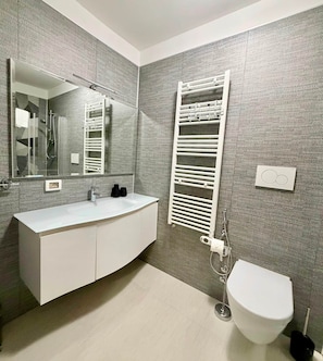 A modern bathroom with a white vanity, a large mirror, a towel rack, and a toilet.