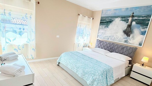 A bedroom with a bed, a bedside table, a nightstand, a window with curtains, a wall-mounted picture, and a ceiling light. - Casa Magenta Apartment 2 (Valeggio sul Mincio)