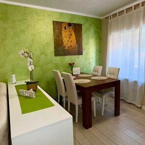 A dining area with a table set for four, a green wall, and a painting above the table.