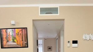 A hallway with beige walls, a tiled floor, and a painting of a colorful street scene. There are light switches and a thermostat on the walls. - Casa Magenta Apartment 2 (Valeggio sul Mincio)