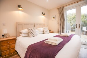 A hotel room with a bed, a nightstand, a lamp, a window with curtains, and a view of the outdoors. - The Old Farmhouse · Stunning farmhouse in Cambridgeshire countryside (Sawtry)