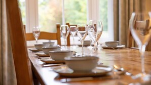 A dining table set with bowls, plates, and wine glasses, with a view of greenery outside.