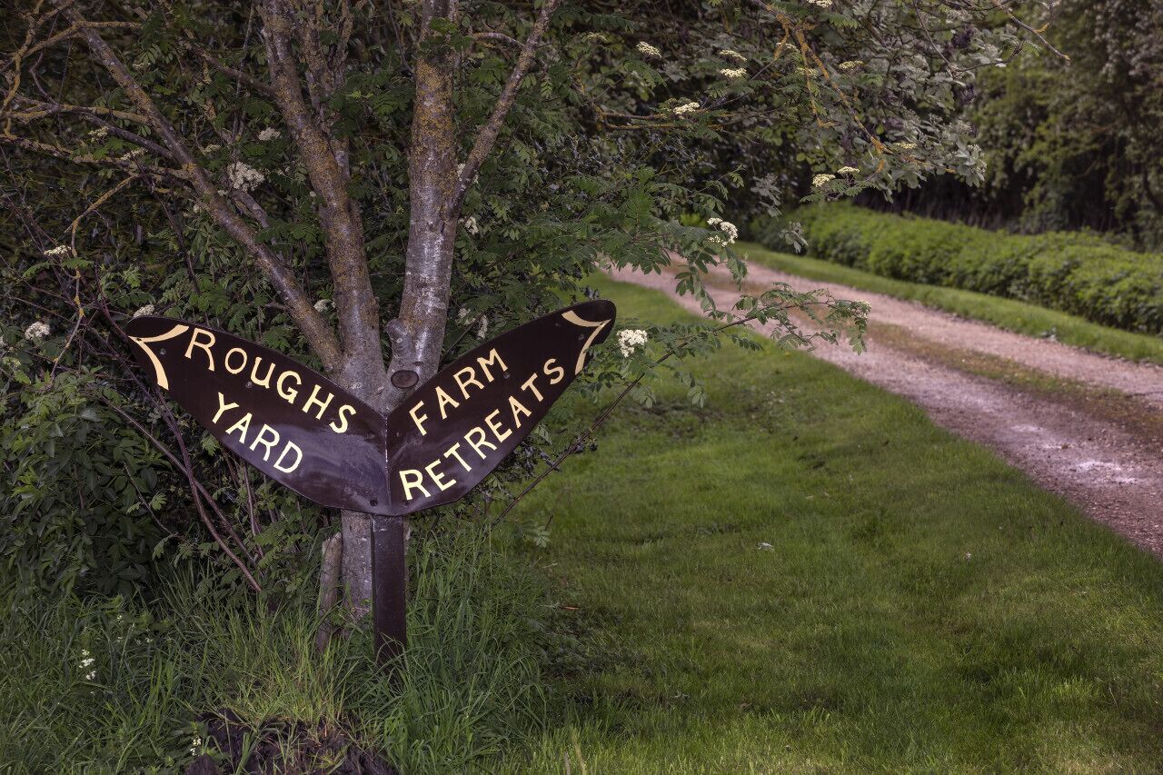 En vejskilte med 'Roughs Yard' og 'Farm Retreats', der peger i hver sin retning.