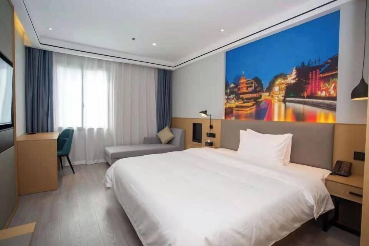 Una habitación de hotel moderna con una cama grande, un escritorio, una silla y una ventana con cortinas.