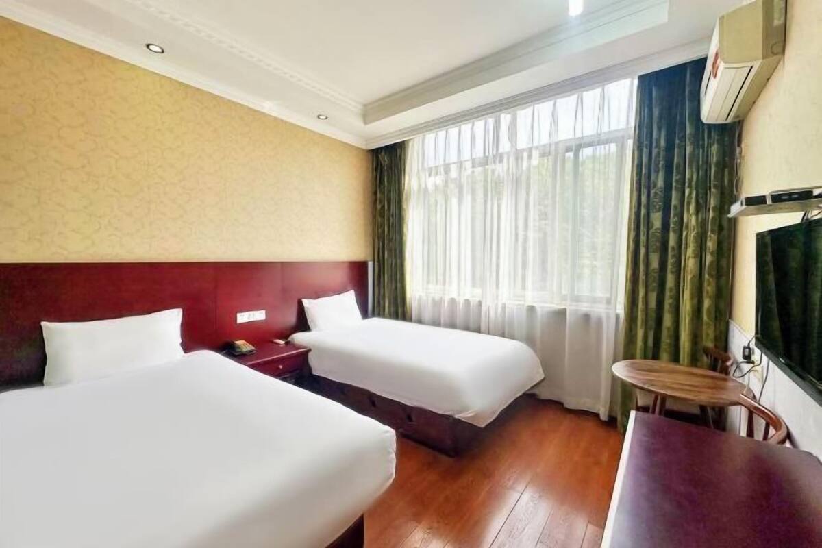 Habitación de hotel con dos camas, suelo de madera, una mesita y una ventana con cortinas.