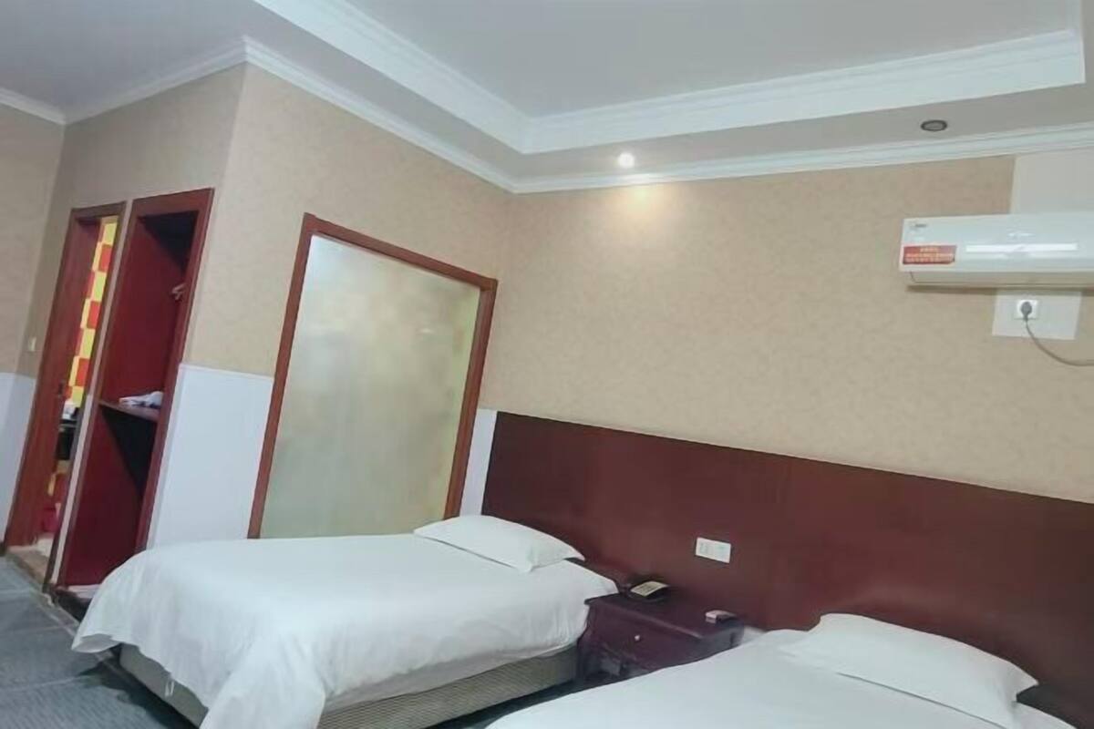 Una habitación de hotel con dos camas, un armario y un equipo de aire acondicionado en la pared.