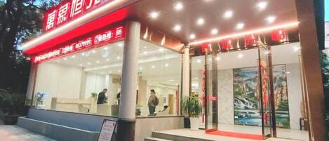 A hotel entrance with a red awning, a reception desk, and a staircase leading to the entrance.