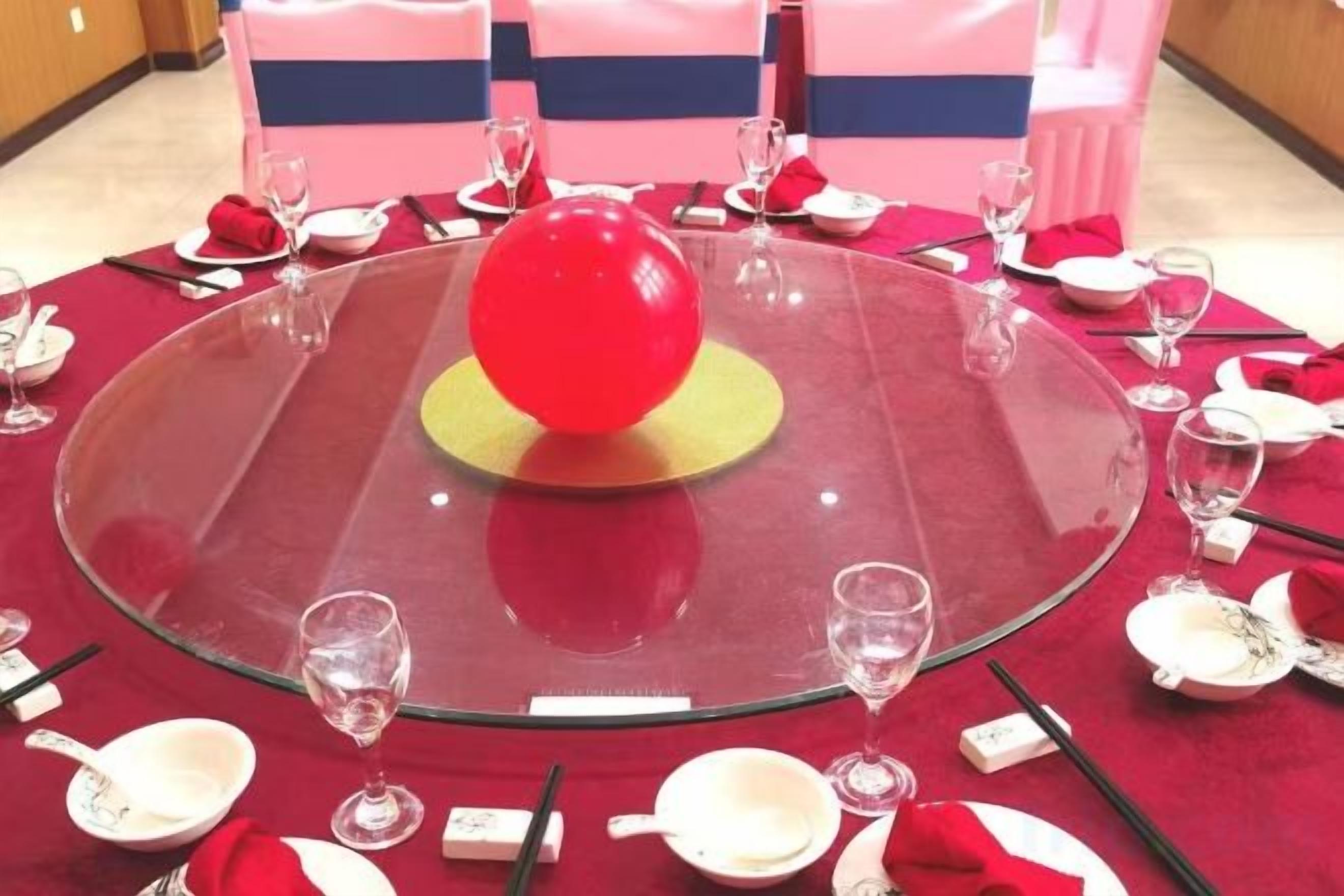 Ein runder Tisch mit transparenter Glasplatte, umgeben von Geschirr in Rot und Weiß, und einer roten Ballongestaltung in der Mitte.