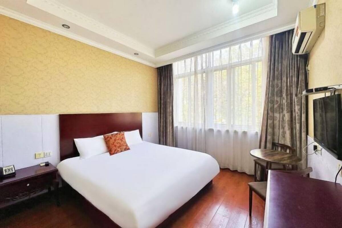 Una habitación de hotel con una cama grande, una mesita, un televisor y una ventana con cortinas.