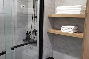 A modern bathroom with a glass-enclosed shower, a towel rack, and a shelf with folded towels. - Vientiane Hengyuan Hotel (Nanjing Jianning Road Railway Station) (Nanjing)