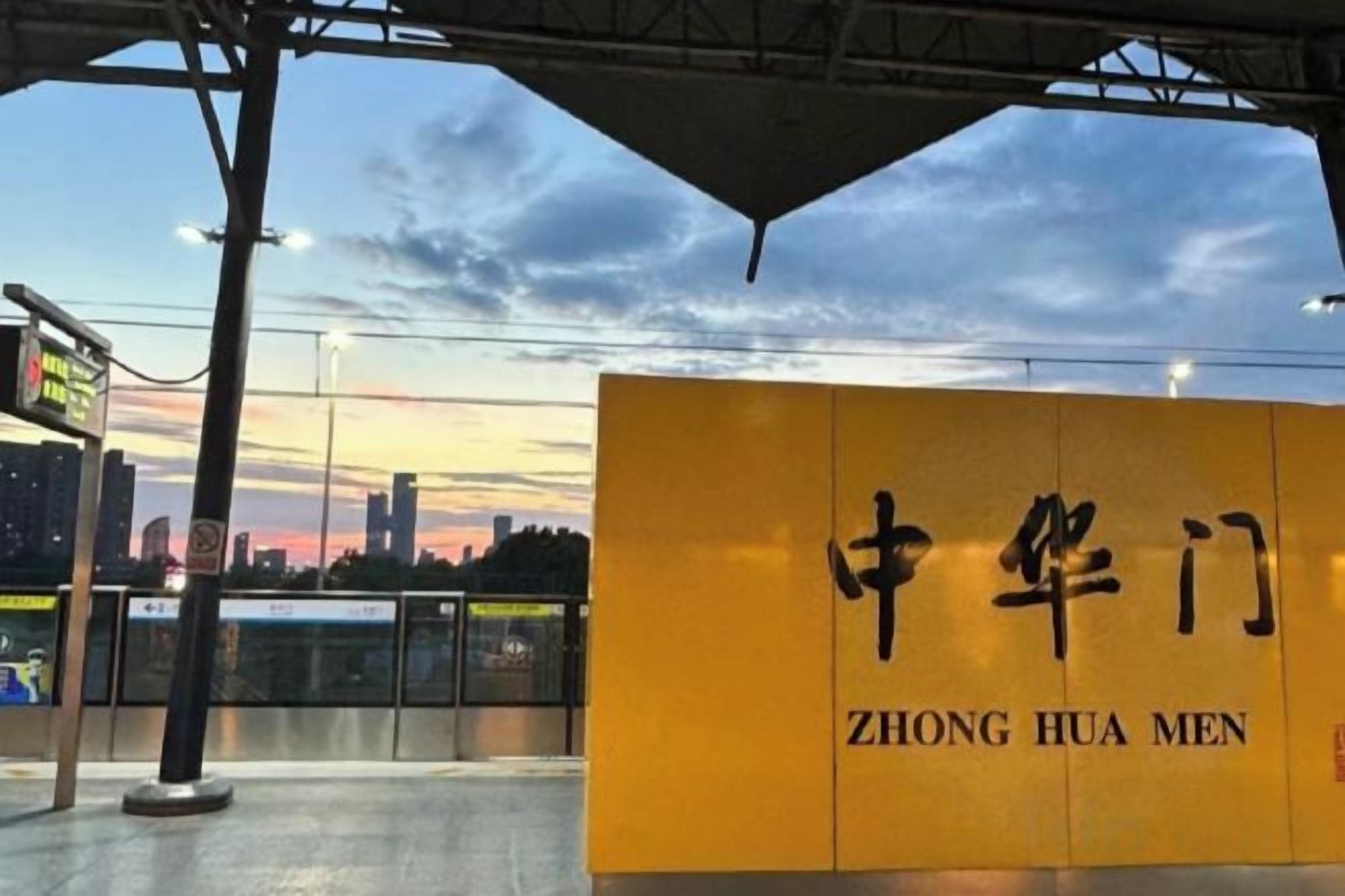 Et gult skilt med kinesiske tegn og engelsk tekst 'ZHONG HUA MEN' på en perron på en togstation.