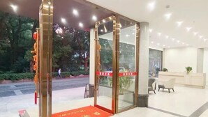Un hall de hotel con mostrador de recepción, zona de estar y puerta de cristal de entrada.