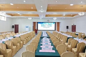 Une salle de conférence avec des rangées de chaises, des tables portant des plaques nominatives et un écran de présentation.