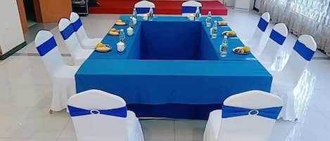 A conference room with a blue table, white chairs with blue sashes, and a projector screen.