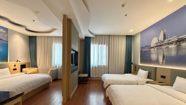 Habitación de hotel con dos camas, una zona de estar, un televisor y un cuadro de un edificio.