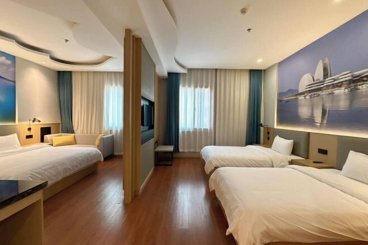 Habitación de hotel con dos camas, una zona de estar, un televisor y un cuadro de un edificio.