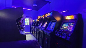 A row of arcade machines in a dimly lit room with purple lighting. - Eagle’s Landing (Lock Haven)
