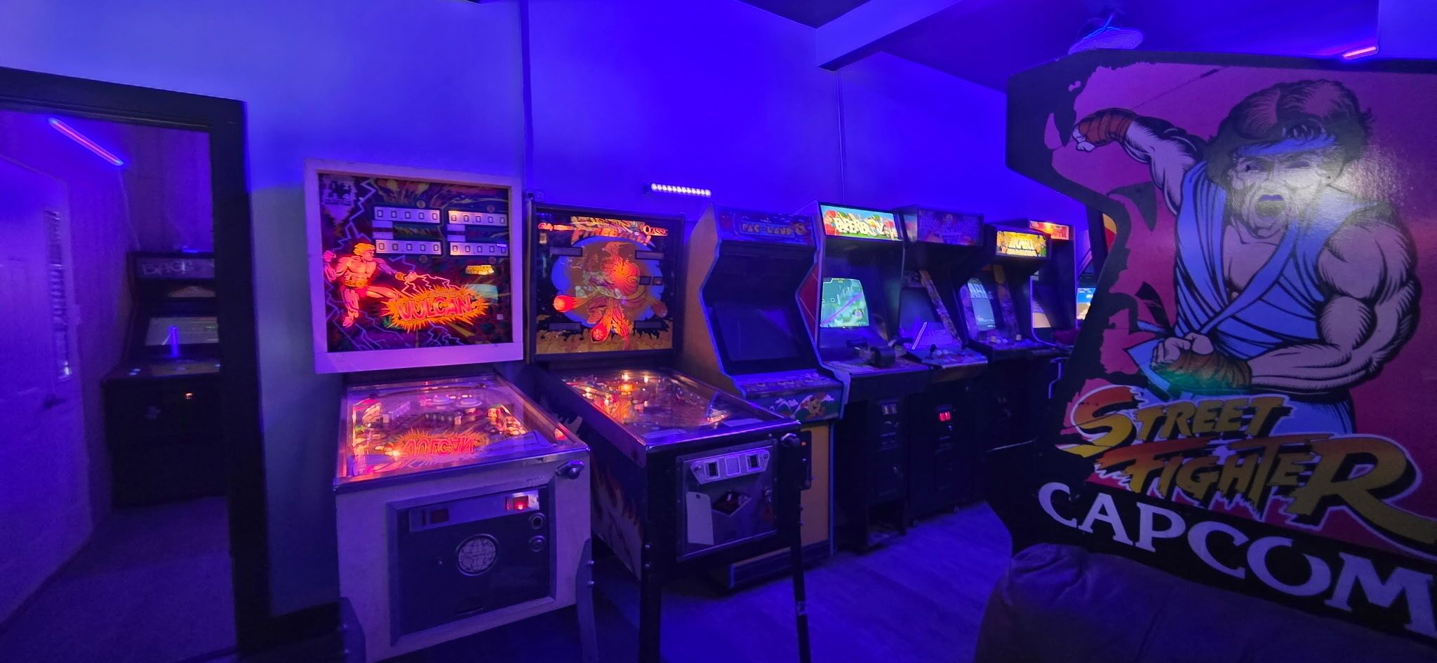 Een kamer met speelautomaten, waaronder een Street Fighter II Capcom spel, en een muurschildering van een gespierde figuur.
