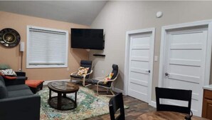 A living room with a sofa, two armchairs, a coffee table, a TV mounted on the wall, and two white doors. - Eagle’s Landing (Lock Haven)