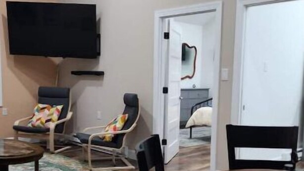 A living room with a wooden floor, a TV mounted on the wall, a dining table with chairs, and a door leading to another room. - Eagle’s Landing (Lock Haven)