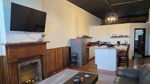 A living room with a fireplace, a television mounted on the wall, a kitchen area with a microwave, stove, and refrigerator, and a dining area with a table and chairs. - The Delaney's Saloon (Vevay)