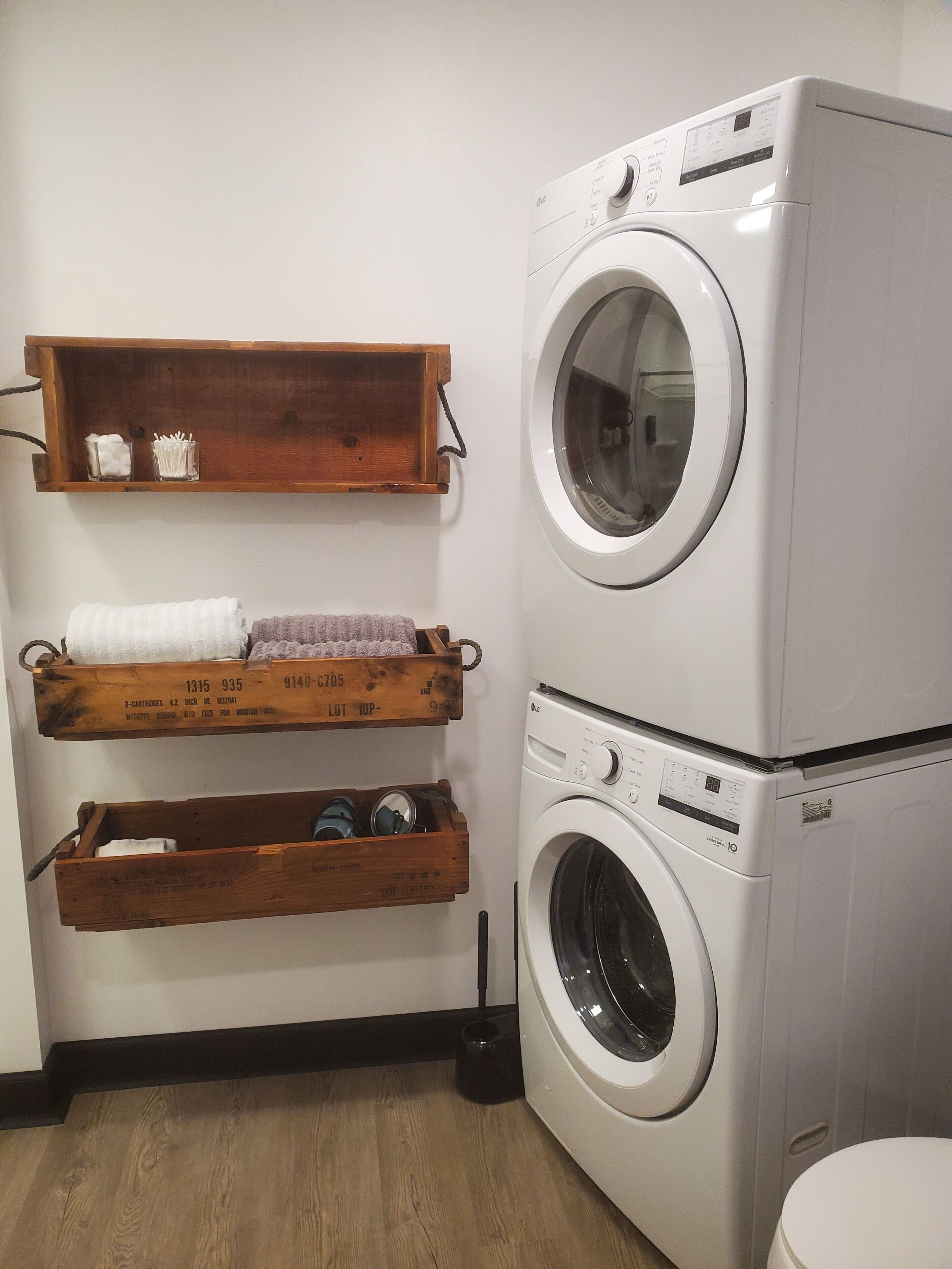Un espace buanderie équipé d’un lave-linge à chargement frontal et de deux étagères en bois situées au-dessus.