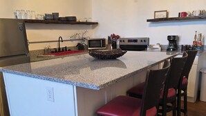 A kitchen with a central island, bar stools, a microwave, and a coffee maker. - The Delaney's Saloon (Vevay)