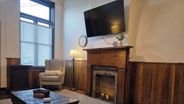 A living room with a fireplace, a television mounted on the wall, a sofa, and a coffee table. - The Delaney's Saloon (Vevay)