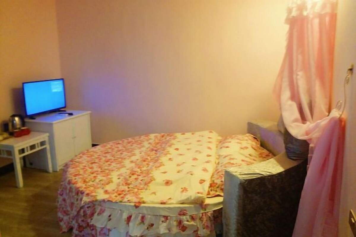 Une chambre à coucher avec un lit, un bureau avec un ordinateur et une fenêtre avec des rideaux.