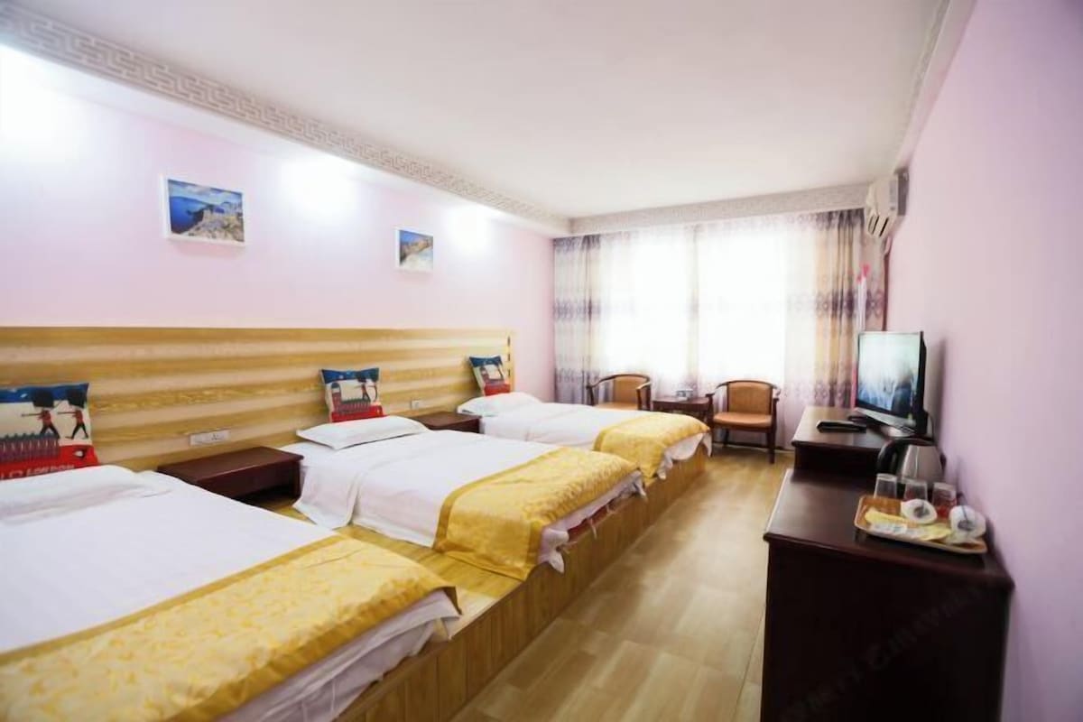 Une chambre d’hôtel avec trois lits, une télévision et un bureau sur lequel se trouve un plateau de collations.