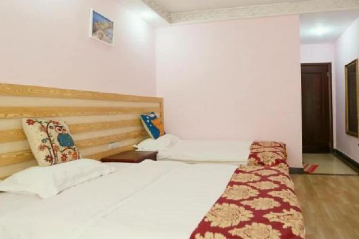 Une chambre avec deux lits, des têtes de lit en bois et une couvre-lit rouge à motifs.