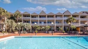 A hotel with a pool, multiple balconies, and palm trees.