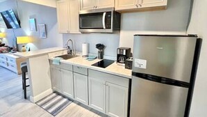 A modern kitchen with white cabinets, a stainless steel refrigerator, a microwave, and a sink.