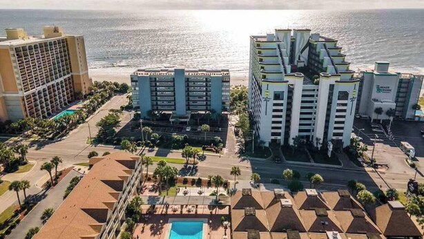 A coastal hotel complex with multiple buildings, a swimming pool, and a beach view.