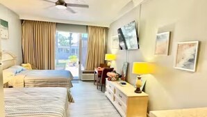 A hotel room with two beds, a desk, a chair, a dresser, and a ceiling fan.