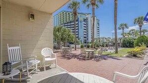 An outdoor patio area with white chairs and tables, palm trees, and a view of a high-rise building.
