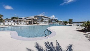 Ein Poolbereich eines Resorts mit blauem Himmel, einem großen Gebäude im Hintergrund und einer Palme im Vordergrund.