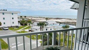 Ein Balkon mit Blick auf einen Strand, ein Schwimmbad und ein Gebäude mit weißer Fassade.