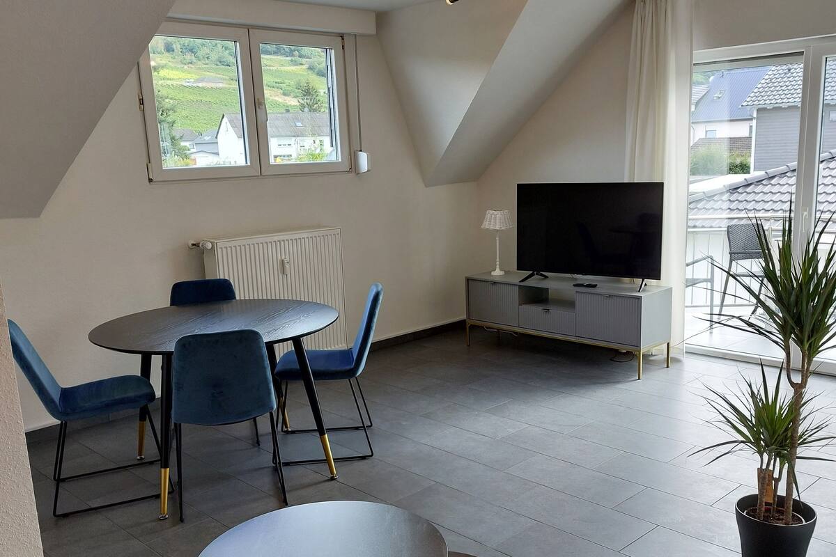Una sala de estar moderna con comedor, televisor de pantalla plana y un ventanal con vistas al exterior.