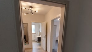 A hallway with a wooden floor leading to a bathroom and a bedroom.