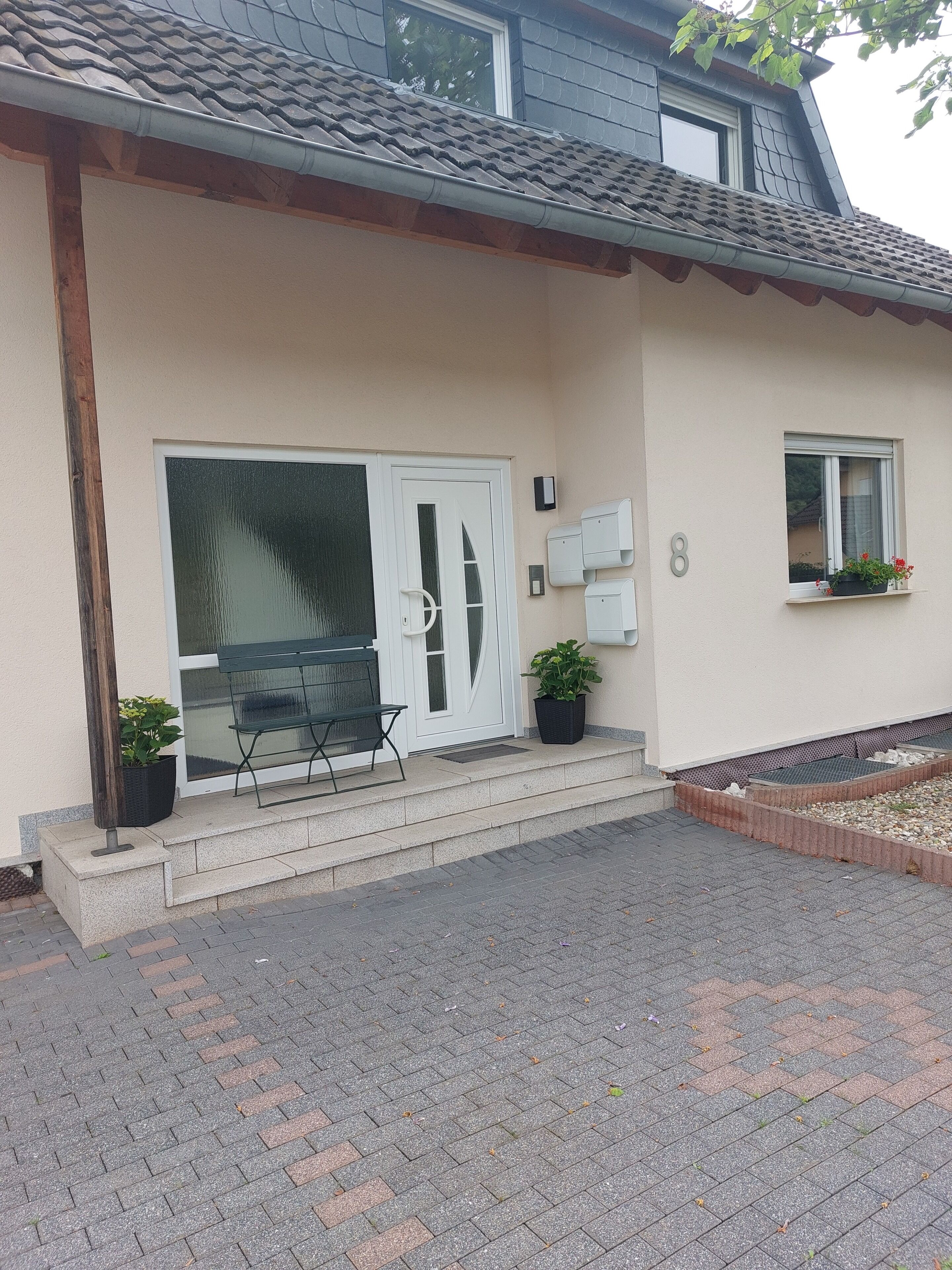 Ein Haus mit weißer Tür, einer kleinen Veranda und einem Fenster mit Pflanzen.