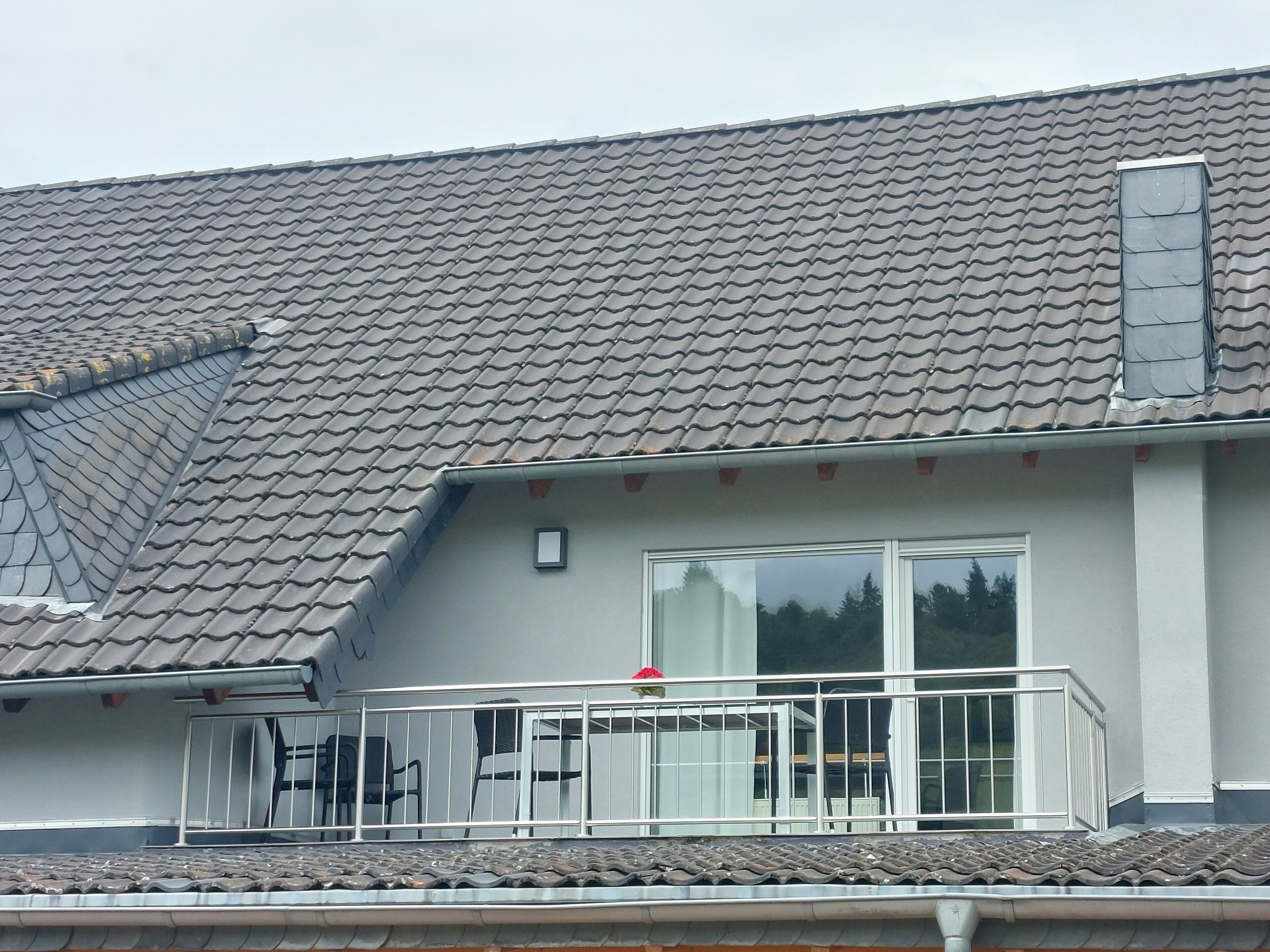 Een woongebouw met een pannendak, een balkon met een hekwerk en een raam.