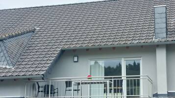 Een woongebouw met een pannendak, een balkon met een hekwerk en een raam.