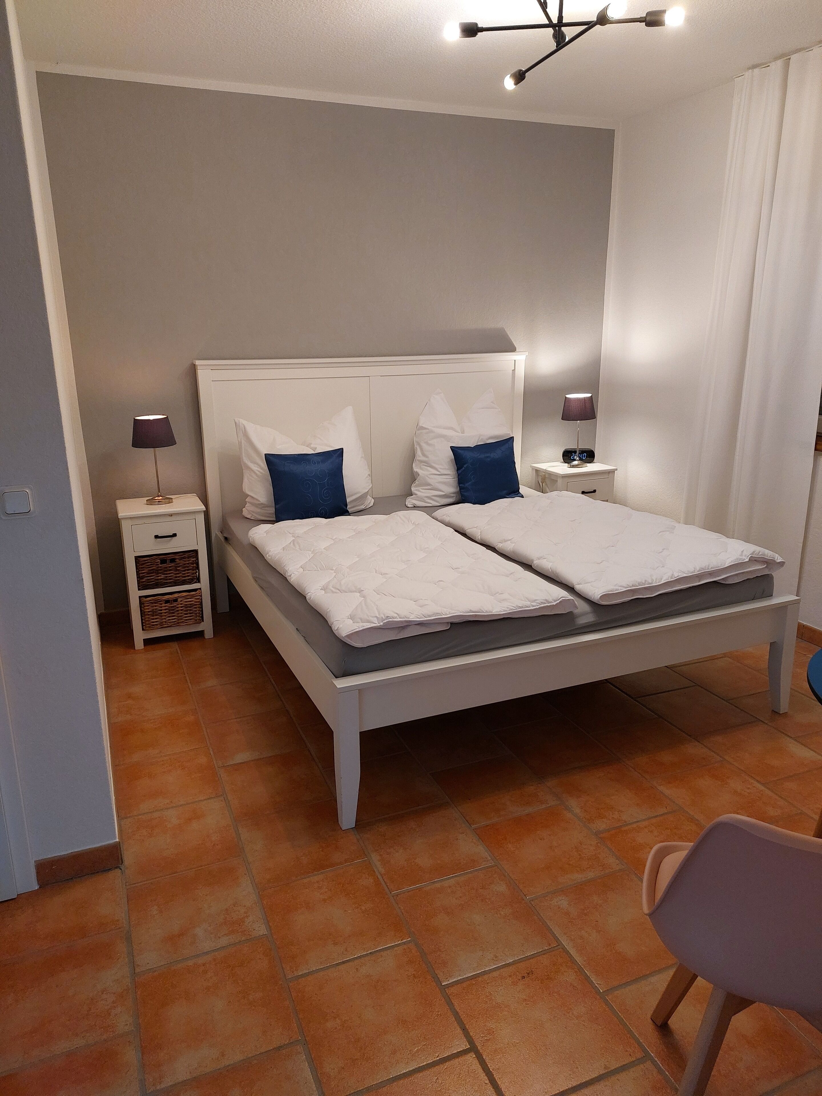 Un letto matrimoniale con biancheria da letto bianca e cuscini blu, un comodino con una lampada e una piccola cassettiera.