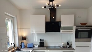 A modern kitchen with white cabinetry, a built-in oven, a coffee maker, and a pendant light fixture.