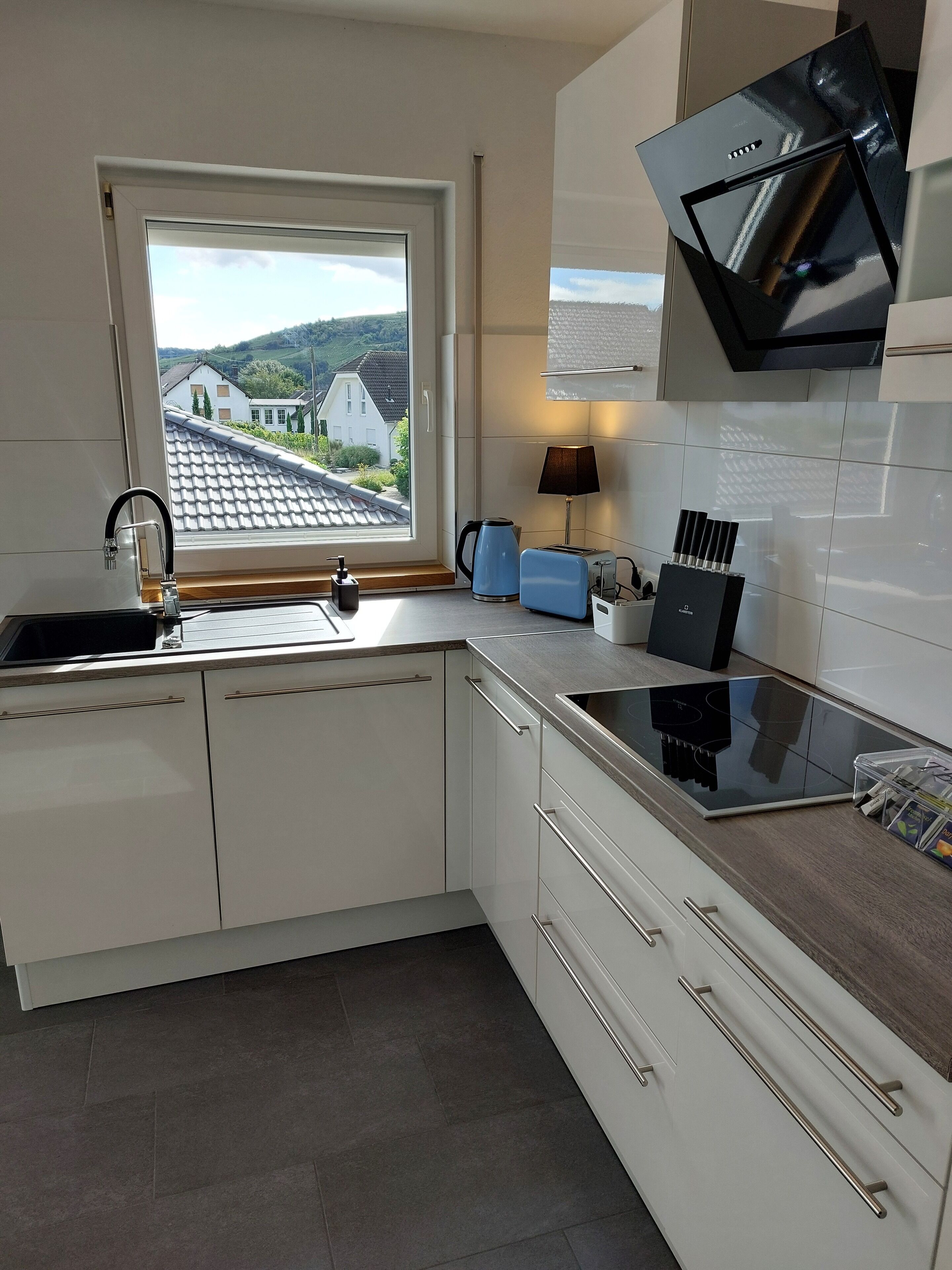 A modern kitchen with white cabinets, a black stove, and a window overlooking a residential area.
