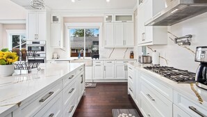 Cocina moderna con armarios blancos, una isla central, estufa a gas y una lámpara colgante.