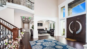 Amplia sala de estar con una escalera de madera, un tapete grande de color azul con diseño y una puerta de madera oscura.