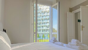 Habitación de hotel con una cama grande, vista a un edificio desde la ventana y un balcón con barandilla.