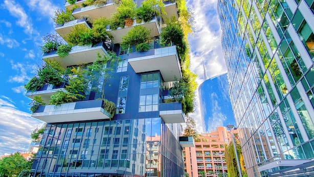 Un edificio moderno con varios balcones cubiertos de vegetación, amplios ventanales de vidrio y una explanada pavimentada.